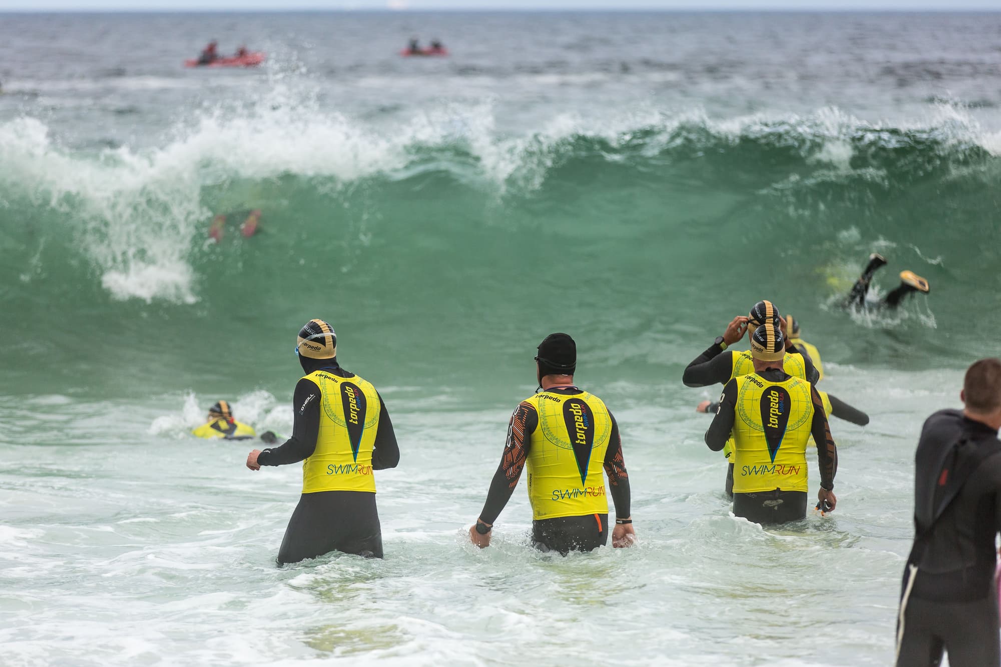 Athletes in yellow Torpedo vests wading into a breaking wave