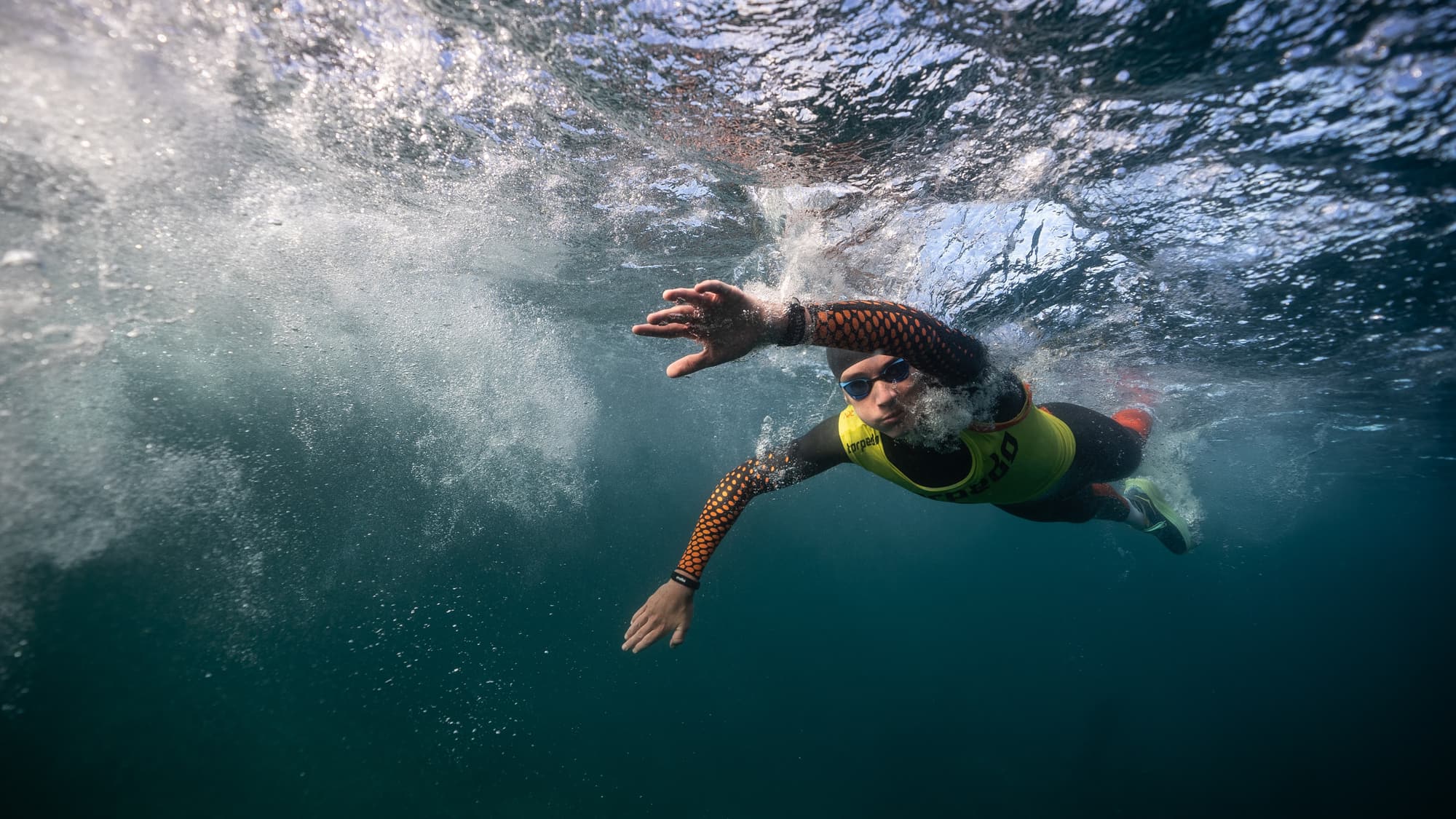 Underwater view of a swimrunner mid-stroke in a yellow Torpedo vest