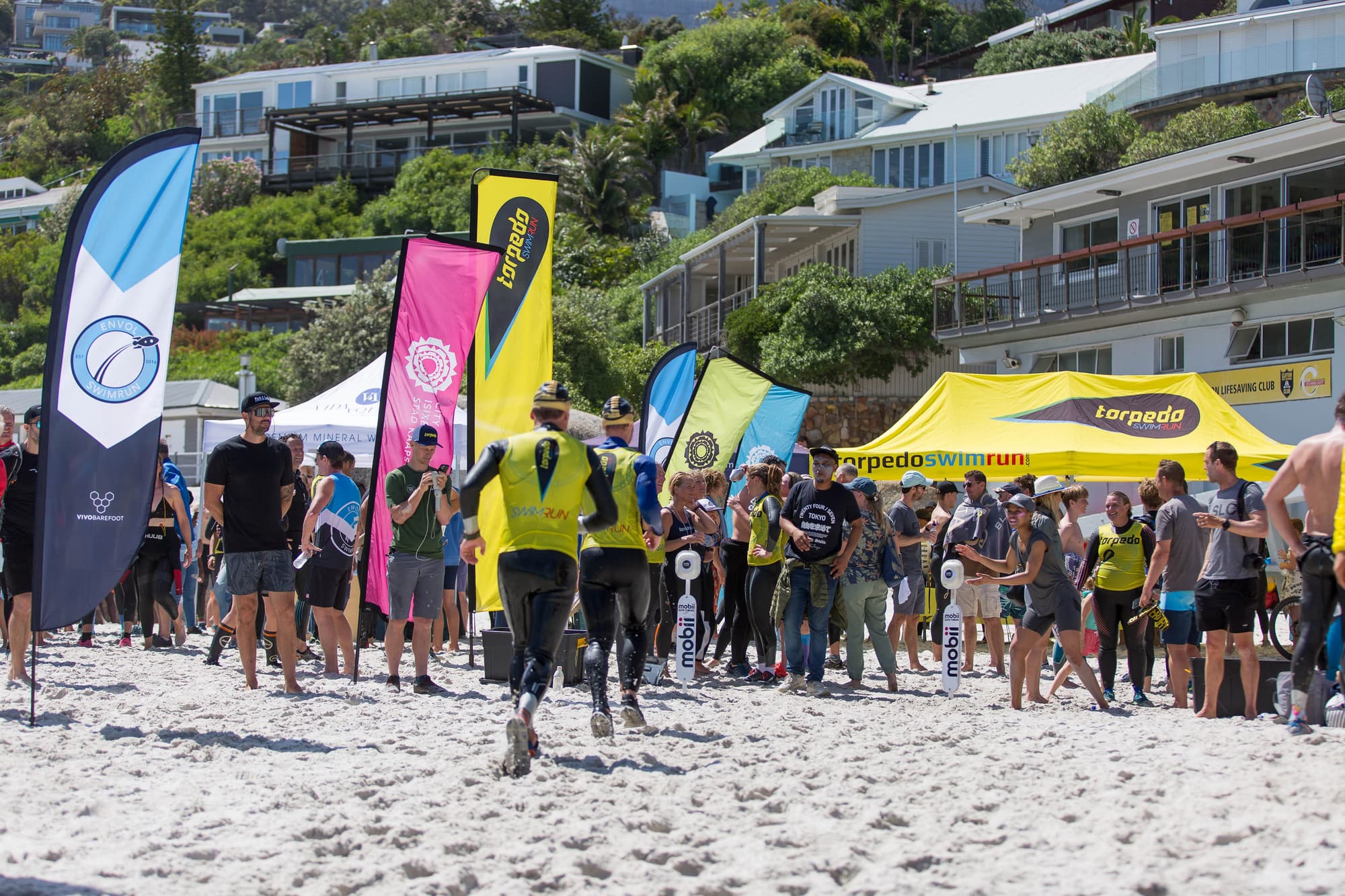 Swimrunners heading through the race village on a busy white-sand beach
