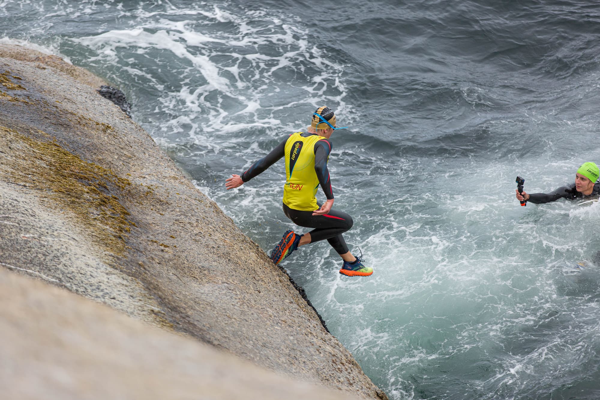 A swimrunner leaping off a granite slab into churning white water