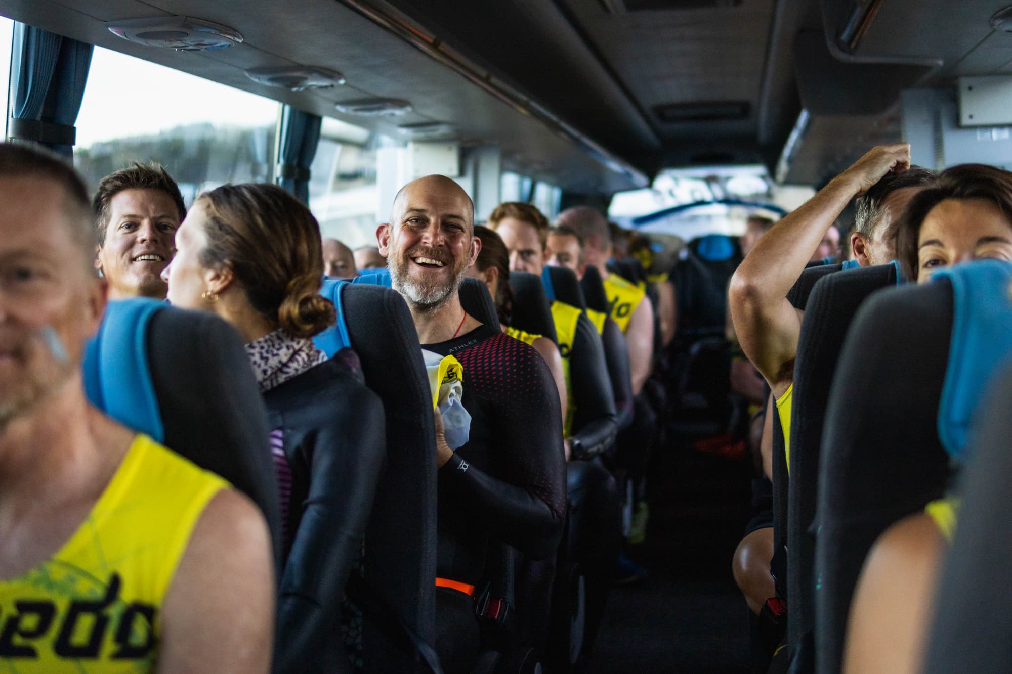 Smiling swimrunners in wetsuits and yellow vests on the bus to the start