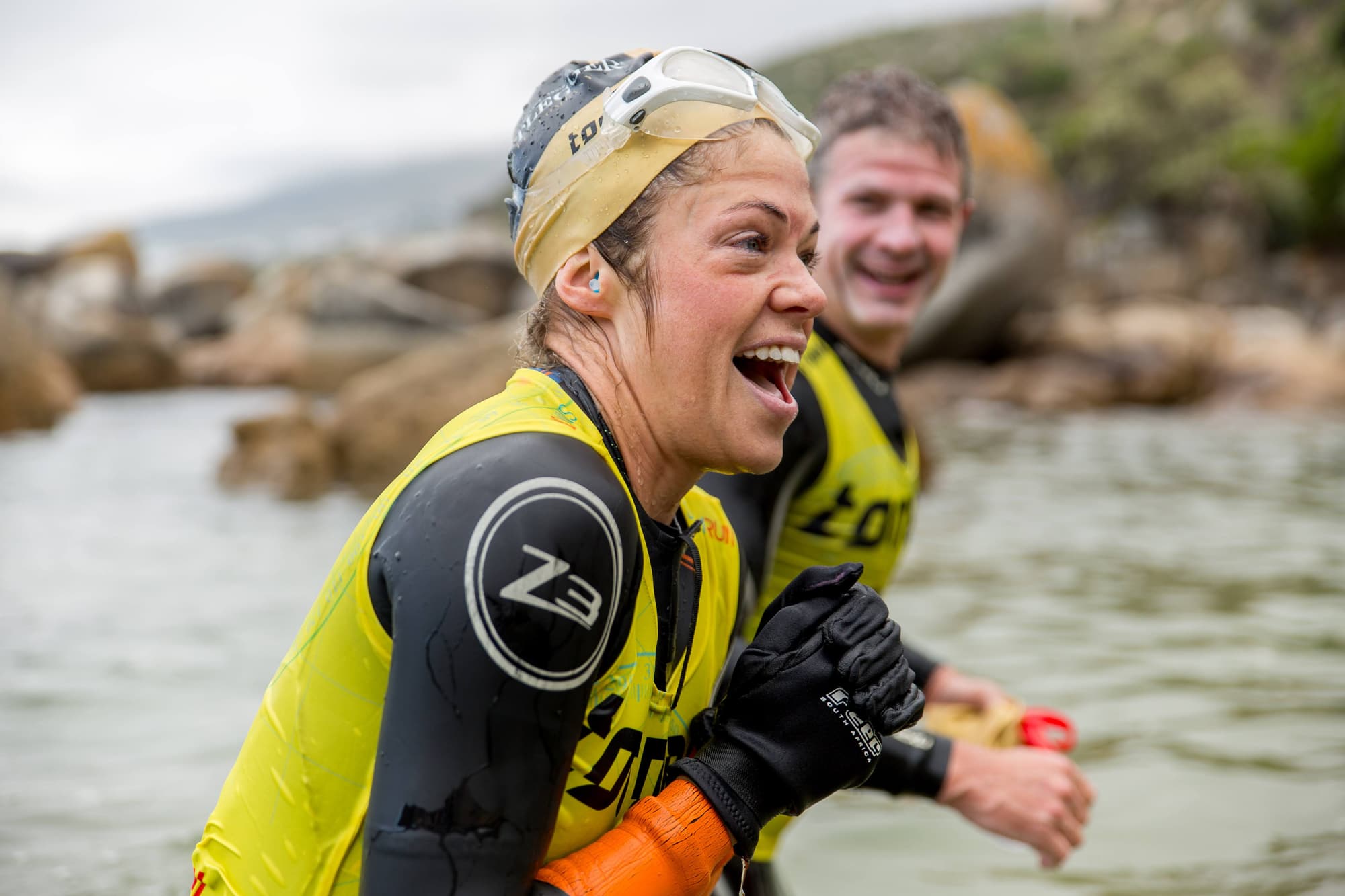 A laughing swimrunner and her teammate climbing out of the water