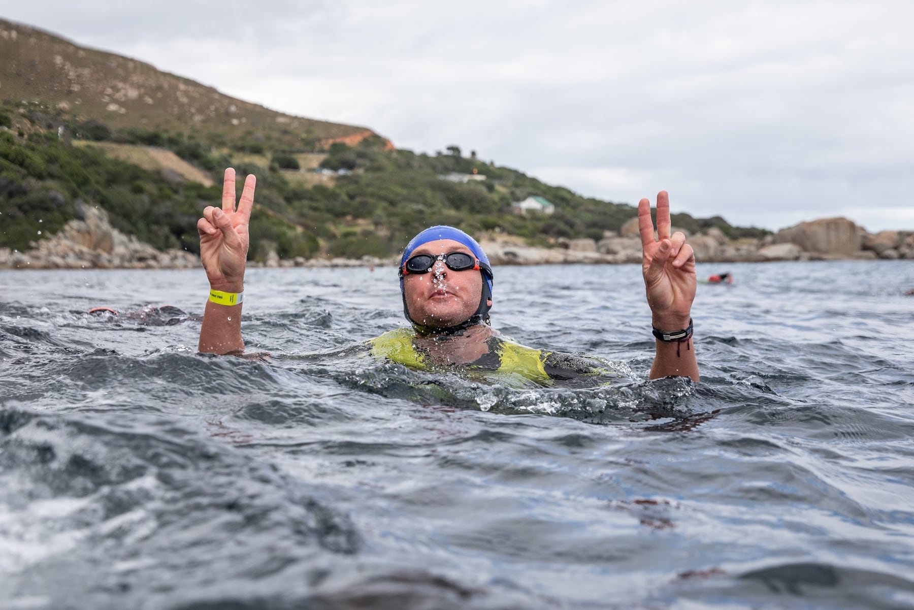 A swimmer in a blue cap flashing peace signs with both hands in the ocean