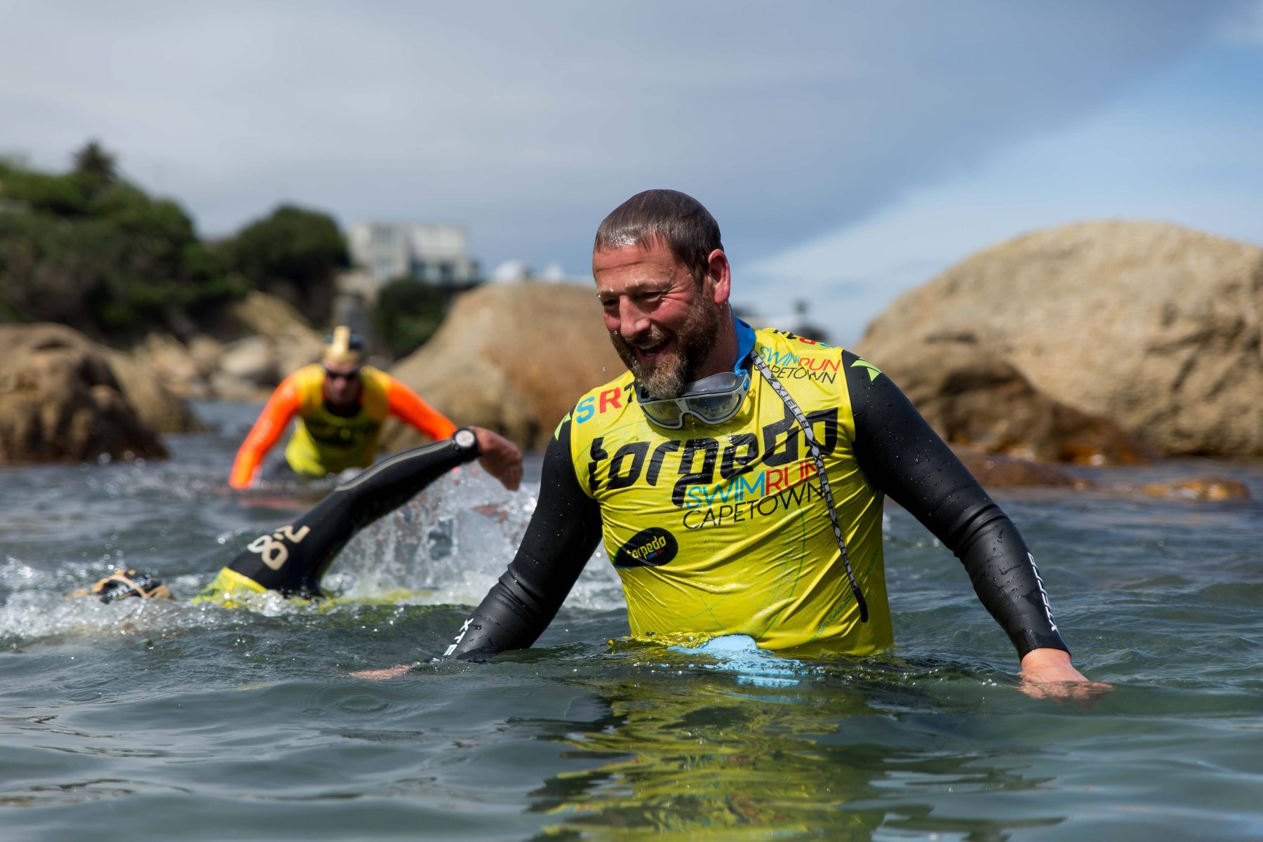 A laughing bearded swimrunner in a Torpedo Swimrun Cape Town top wading through the water