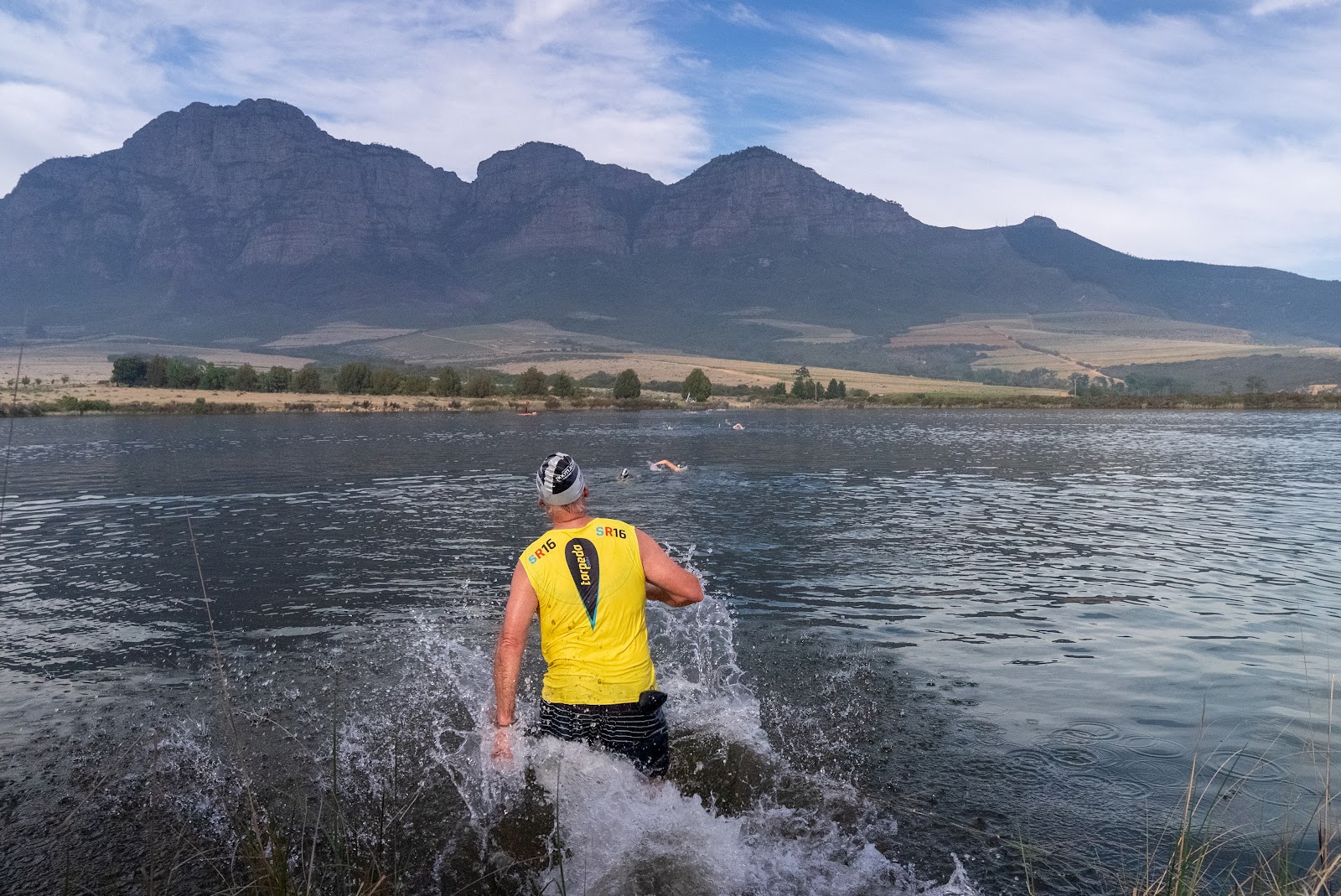 A Torpedo athlete wading out of the Plaisir dam with the Winelands mountains behind, Plaisir 2026