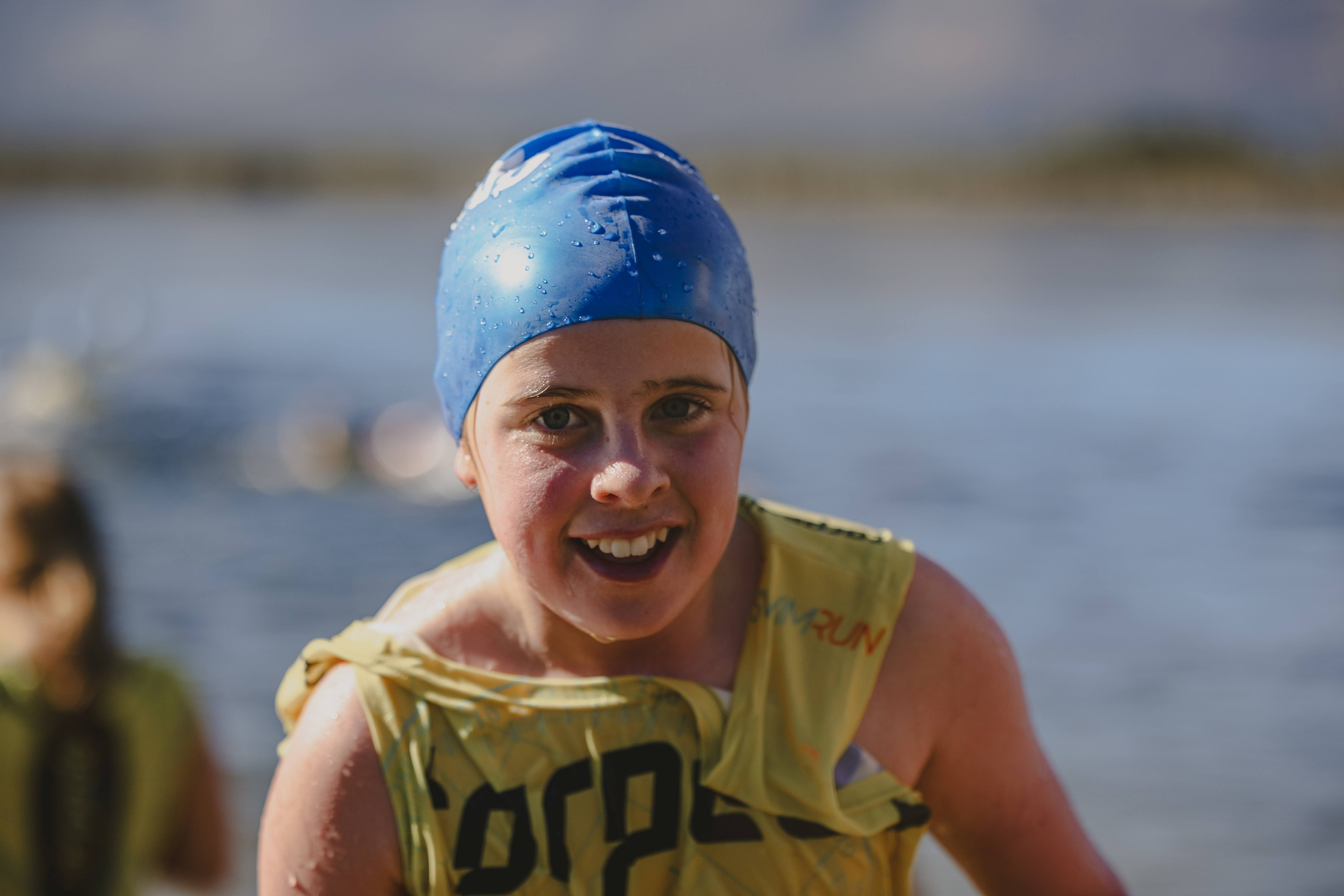 Close-up of a smiling girl in a blue Torpedo cap and yellow vest, water droplets on her cap