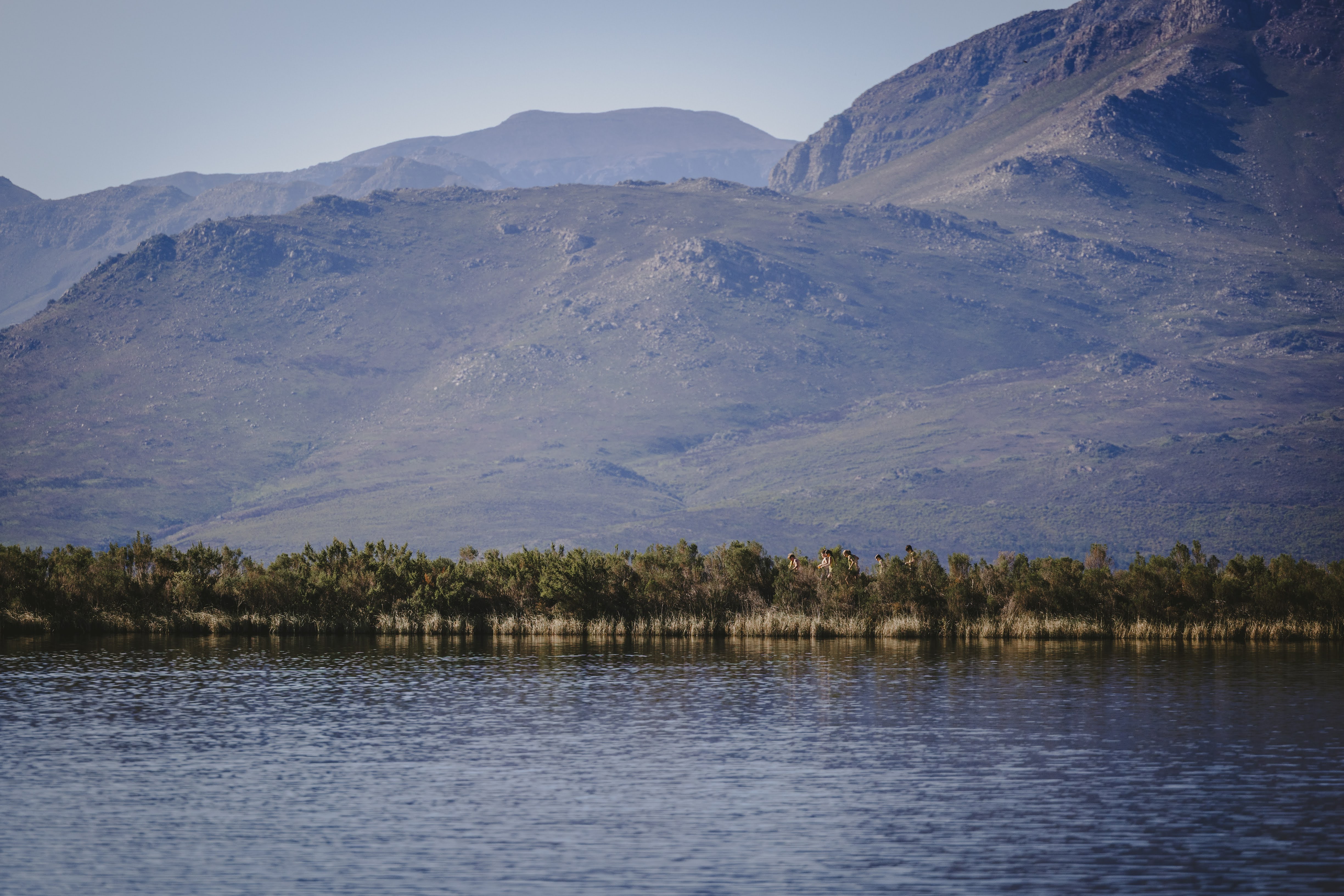 A tiny line of kids running along the far shore of the dam beneath towering mountains