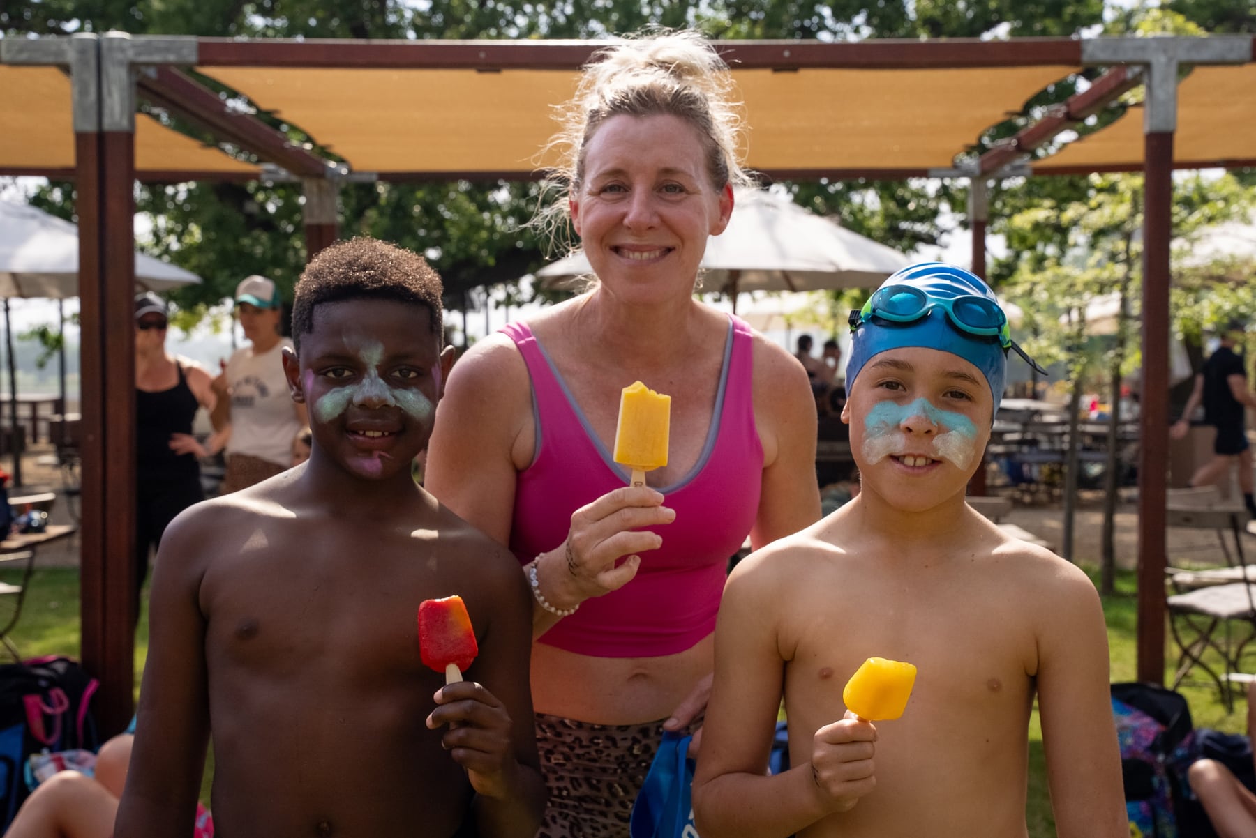 A mom and two face-painted boys smiling with ice lollies in the shade after the race